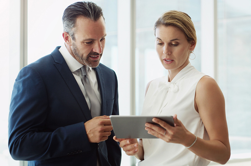 Two business professionals chatting while looking down at a tablet screen